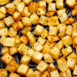 Seasoned golden brown diced potatoes on a black air fryer tray.