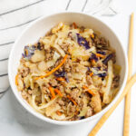 Egg roll in a bowl recipe in a white bowl next to wooden chopsticks and a black and white striped napkin on a white marble surface.