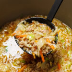 Egg roll soup with ground pork, cabbage, and carrots being lifted out of a pot with a black ladle.