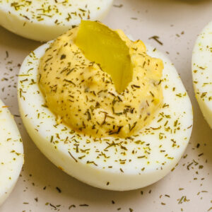 Deviled eggs topped with dill pickle chips on a light gray plate.