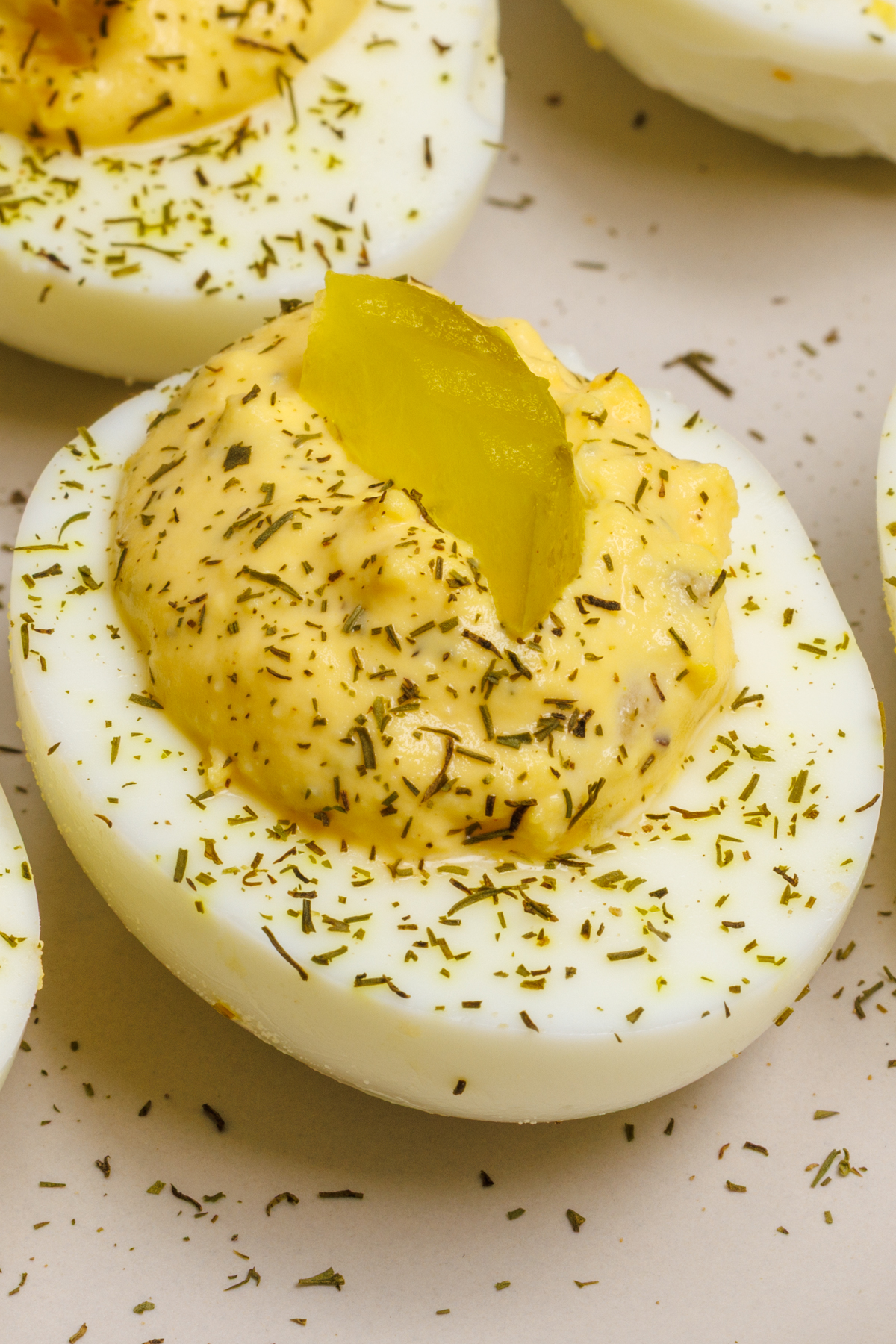 Deviled egg topped with a dill pickle chip on a light gray plate.