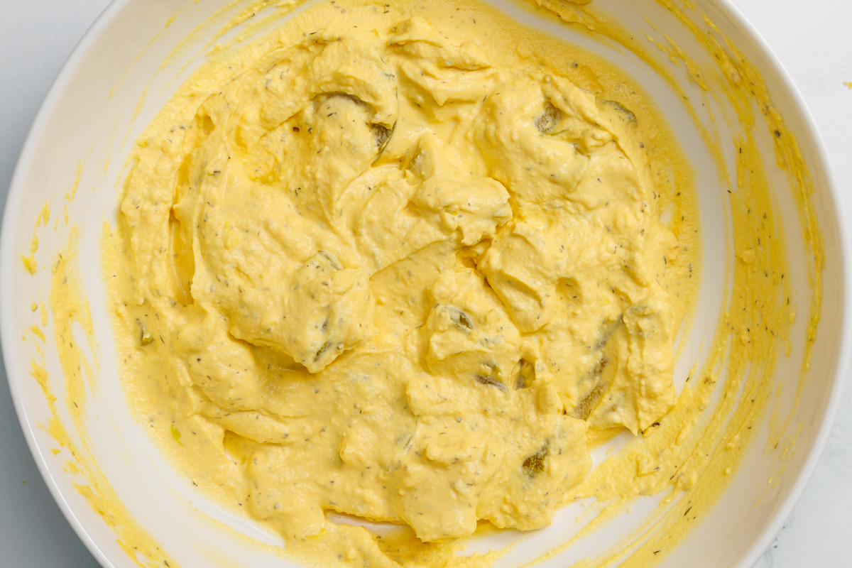Dill pickle deviled egg filling ingredients mixed together in a white bowl.