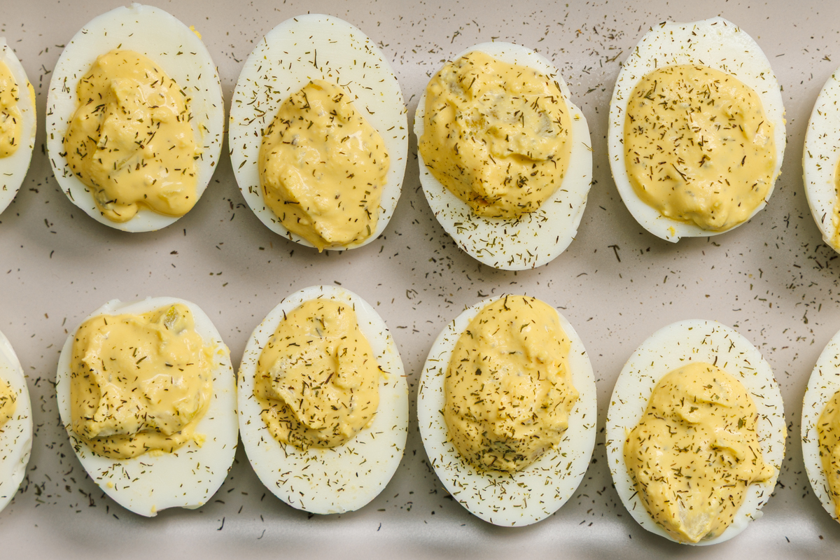 Two rows of dill pickle deviled eggs sprinkled with dried dill on a gray plate.