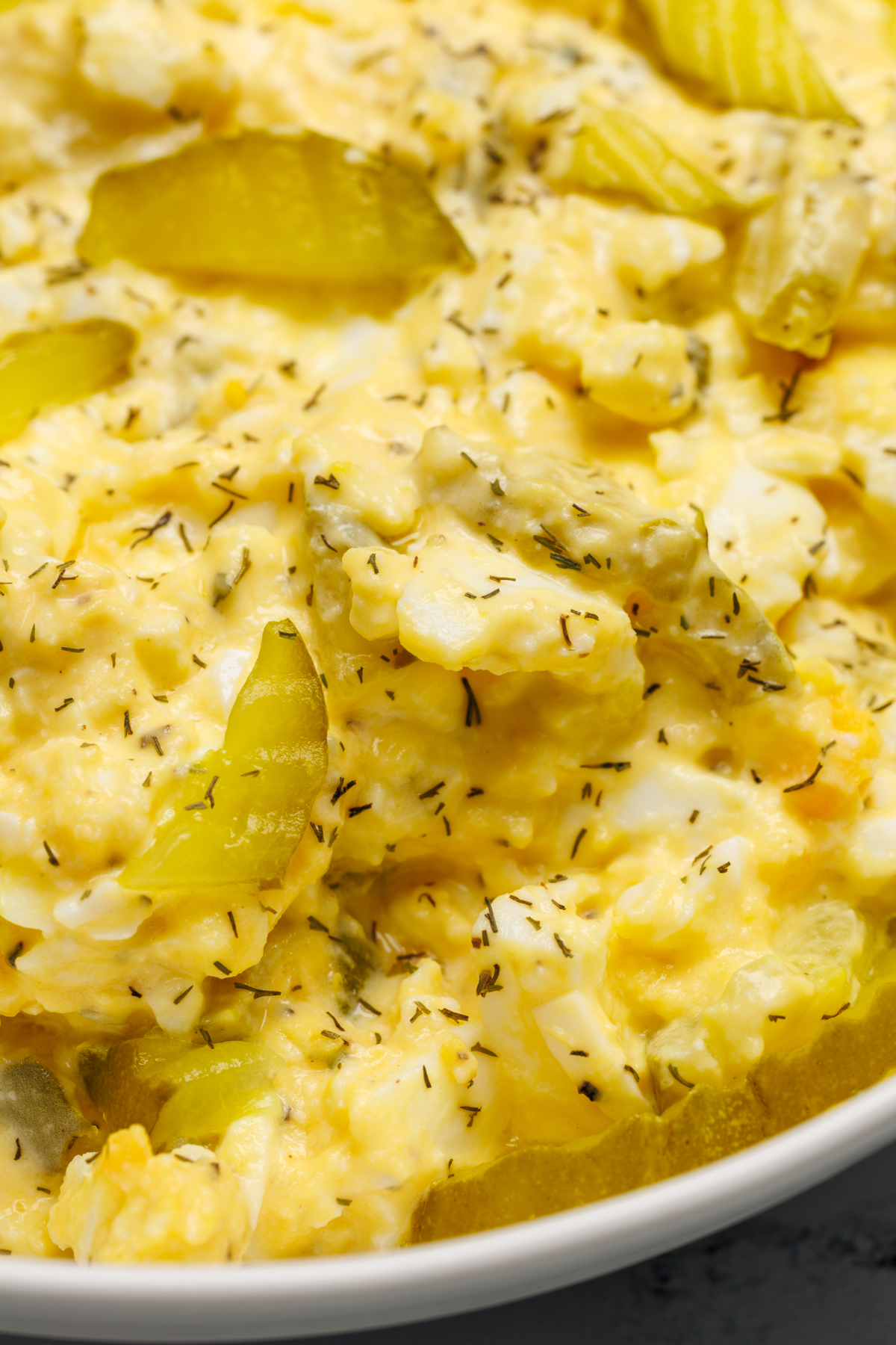 Egg salad with dill pickle chips in a white bowl.