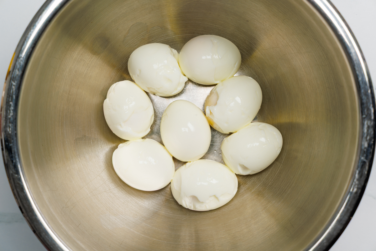 Eight peeled hard boiled eggs in a silver mixing bowl.