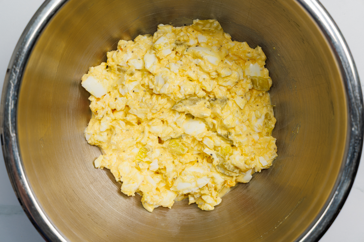 Egg salad ingredients combined in a silver mixing bowl.